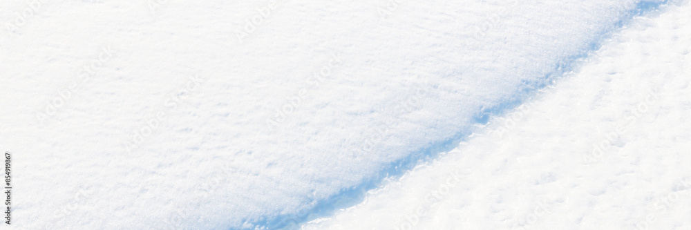 Beautiful winter background with snowy ground. Natural snow texture. Wind sculpted patterns on snow surface. Wide panoramic texture for background and design. Closeup top view with copy space.