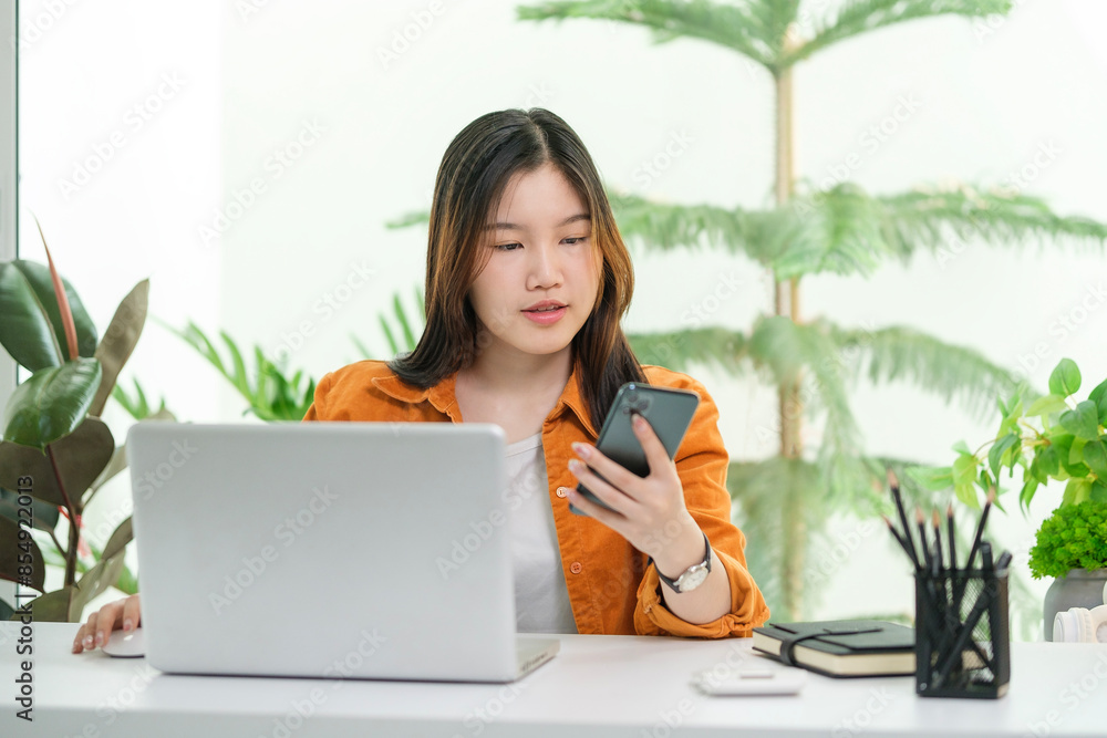 Pretty young woman using mobile phone while working on laptop at home. Pretty young woman using mobile phone while working on laptop at home.