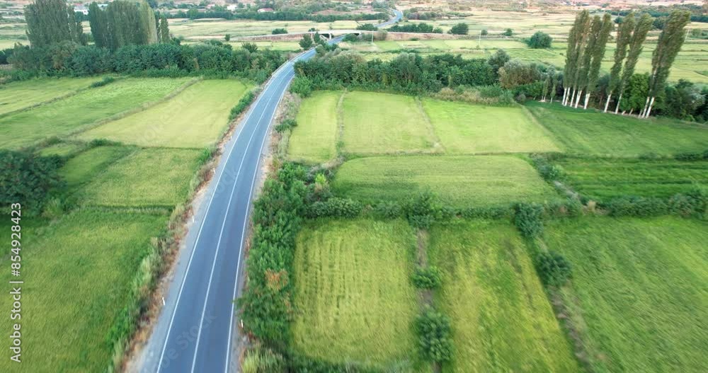 Aerial view of cars driving on a country highway that cuts through agricultural farm fields, with green grass, crops, and trees Aerial view of cars driving on a country highway that cuts through agricultural farm fields, with green grass, crops, and trees