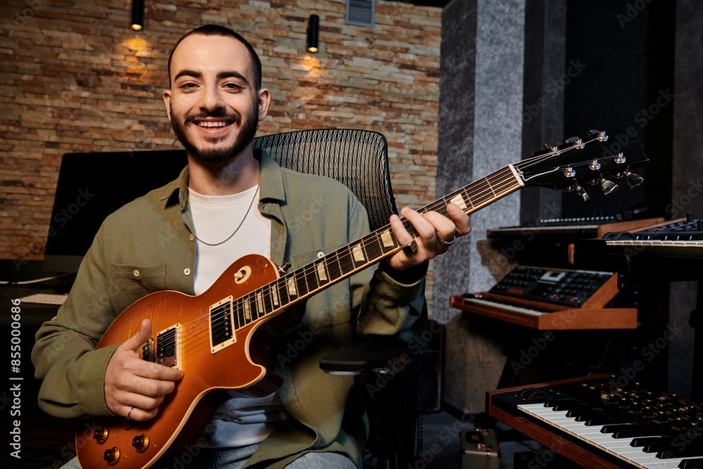 Obraz premium A man joyfully smiles while strumming a guitar in a music band rehearsal at a recording studio.