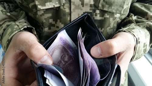 Male hands in military uniform hold money. Ukrainian hryvnia in the hands of a military man. Money against the background of a Ukrainian pixel military uniform.