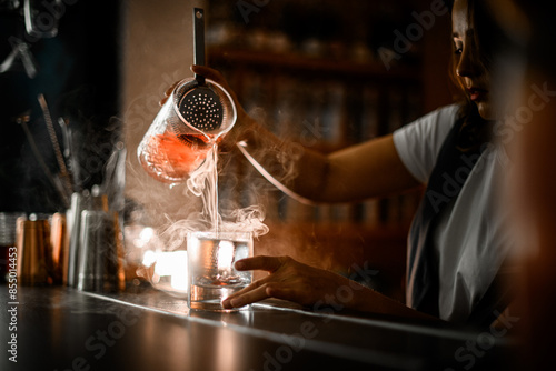 Female bartender pours a brown cocktail with ice from one glass to another