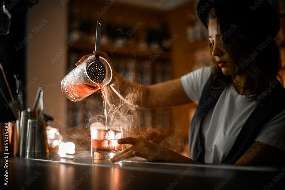 custom made wallpaper toronto digitalWoman bartender in a white t-shirt and vest pours a cocktail with ice from a mixing glass into another glass