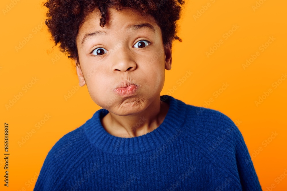 Playful african american boy making a silly face with wide open mouth against a vibrant orange background Playful african american boy making a silly face with wide open mouth against a vibrant orange background