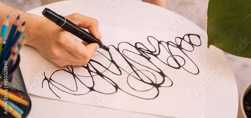Lady draws with a black felt-tip pen on a white sheet. photo