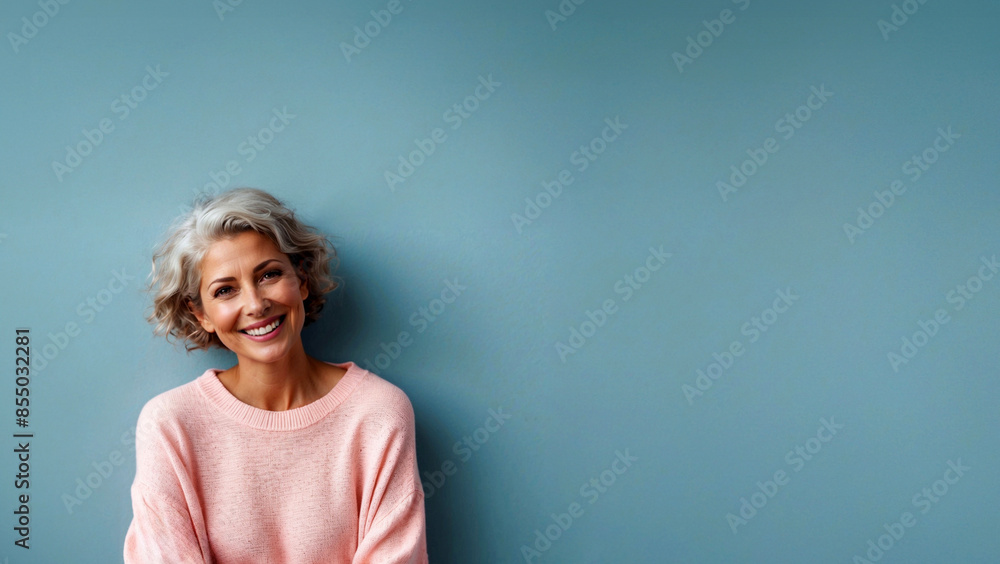 smiling woman in menopause age in pink sweater over a light blue background with copy space smiling woman in menopause age in pink sweater over a light blue background with copy space