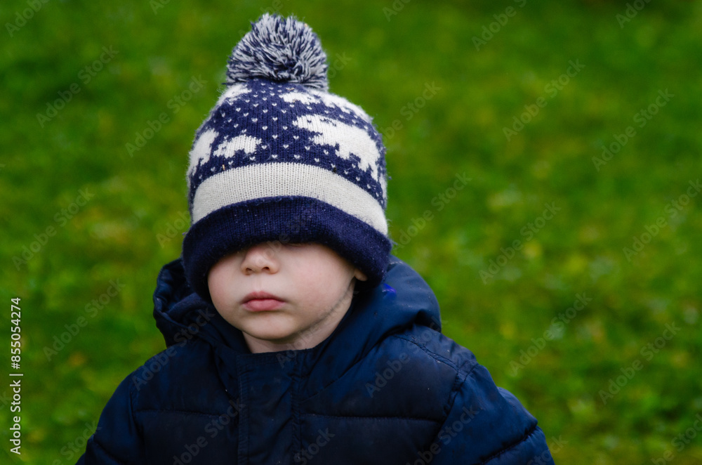 Child wearing a winter hat pulled over their eyes, standing outdoors Child wearing a winter hat pulled over their eyes, standing outdoors