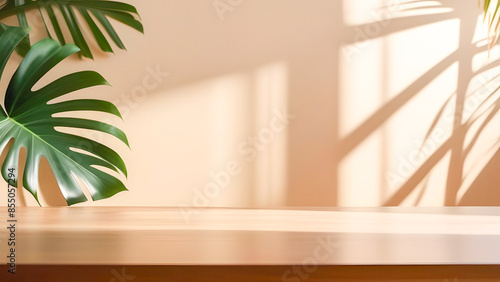 Wooden table counter top with green monstera leaves and beautiful sunlight and shadow on beige wall