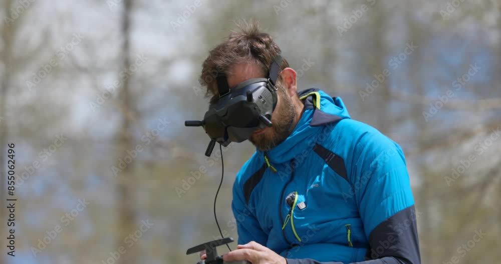 Man in blue jacket using a virtual reality headset and remote control to navigate a drone in an outdoor setting. Man in blue jacket using a virtual reality headset and remote control to navigate a drone in an outdoor setting.