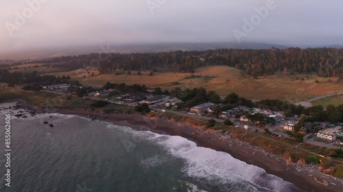 Aerial wide descending shot of oceanfront inns lining Moonstone Beach at sunset in Cambria, California. 4K photo