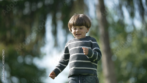 Young Boy Smiling and Running in Striped Sweater in a Wooded Park © Marco