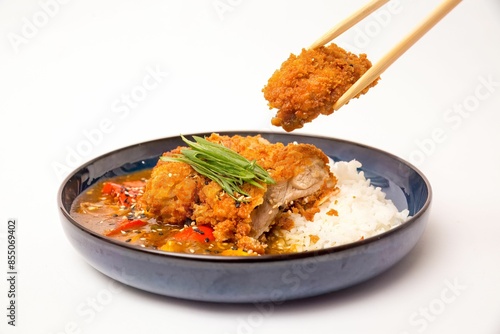 Plate of Japanese katsu curry with rice and chopsticks holding a piece of crispy chicken