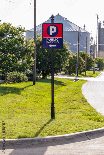 Public parking sign in a grassy area with an industrial backdrop.