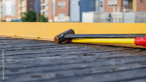 Close-up view of a sledgehammer and a yellow-handled tool resting on a wooden surface train car. Apartments in the background.