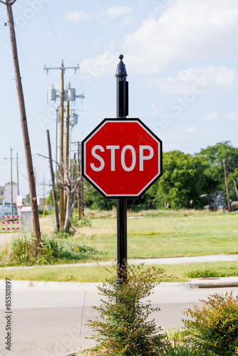 A stop sign on a black post at the edge of a grassy area with an urban background.