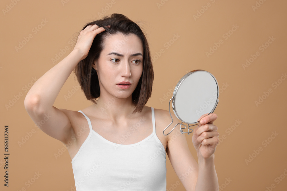 Sad woman with hair loss problem looking at mirror on light brown background Sad woman with hair loss problem looking at mirror on light brown background