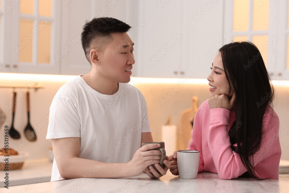 Lovely couple with cups of drink enjoying time together in kitchen