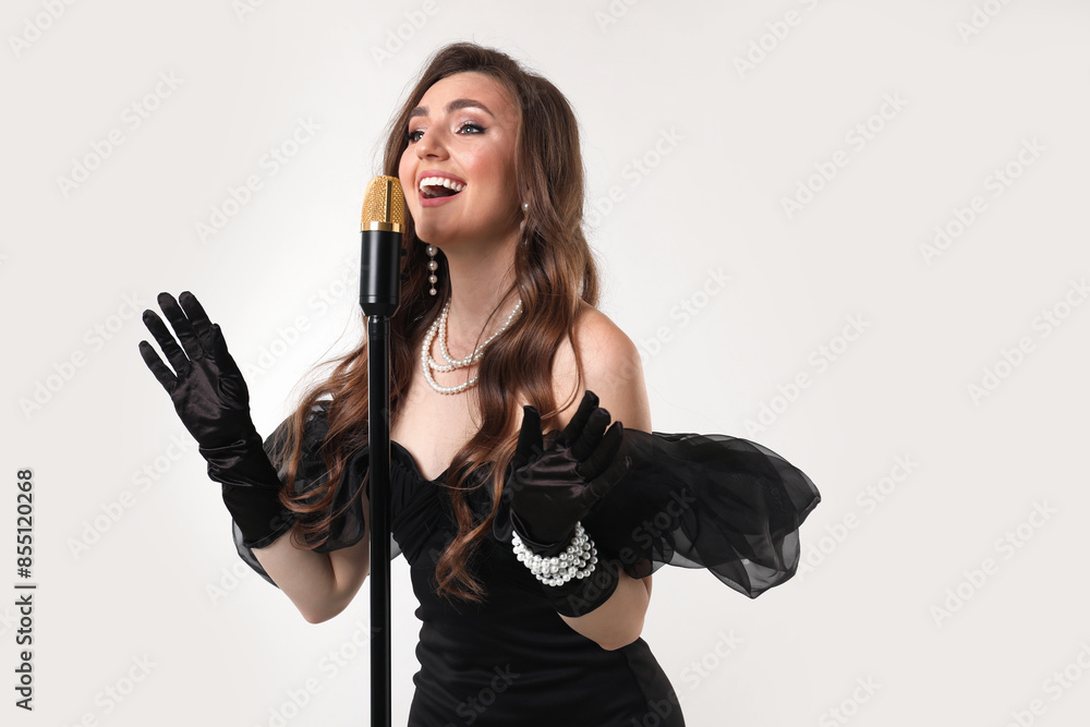 Beautiful young woman in stylish dress with microphone singing on light grey background Beautiful young woman in stylish dress with microphone singing on light grey background
