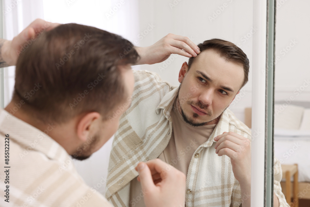 Baldness concept. Sad man with receding hairline looking at mirror indoors Baldness concept. Sad man with receding hairline looking at mirror indoors