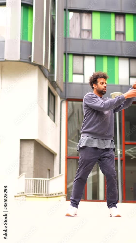 Black ethnic man dancing urban dance in the city in a gray sweatshirt is dancing in front of a building. Scene is energetic and lively Black ethnic man dancing urban dance in the city in a gray sweatshirt is dancing in front of a building. Scene is energetic and lively