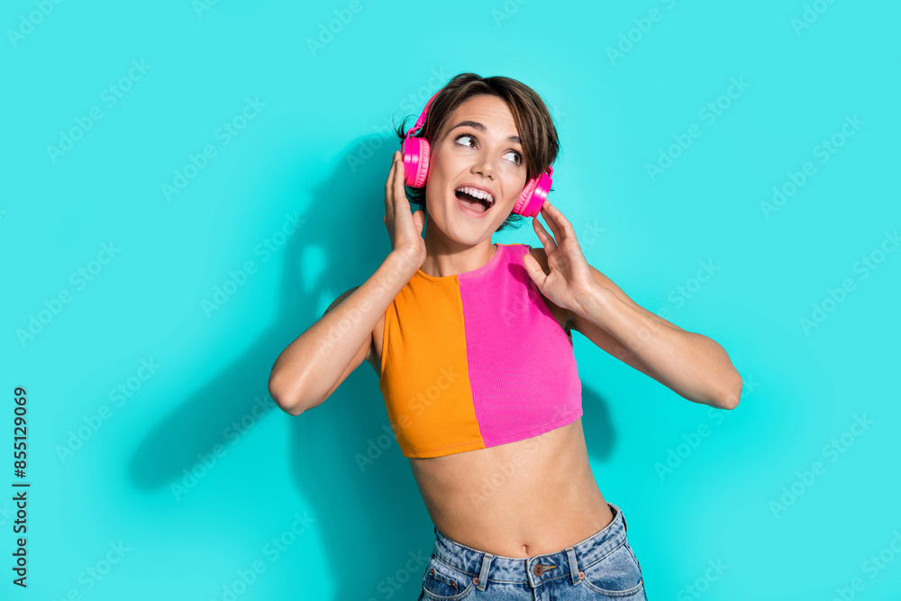 Photo of impressed excited lady dressed colorful top listening songs earphones looking empty space isolated turquoise color background Photo of impressed excited lady dressed colorful top listening songs earphones looking empty space isolated turquoise color background