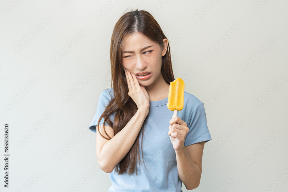 Face expression suffering from sensitive teeth and cold, asian young woman, girl hand touching her cheek, feeling hurt, pain eating ice cream, lolly. Toothache molar tooth at home, dental problem. Face expression suffering from sensitive teeth and cold, asian young woman, girl hand touching her cheek, feeling hurt, pain eating ice cream, lolly. Toothache molar tooth at home, dental problem.
