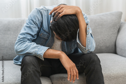Foto Sad upset, frustrated alone asian young man headache thinking about finance problem, difficulty, feeling failure and exhausted, suffering from loneliness sitting on couch at home