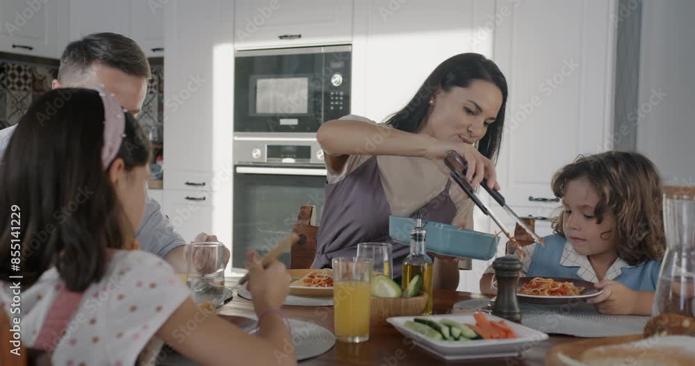 Caring mother serving food to adorable little son having lunch with family husband and children in kitchen at home. People and lifestyle concept. Caring mother serving food to adorable little son having lunch with family husband and children in kitchen at home. People and lifestyle concept.