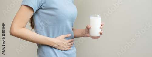 Pain, suffering asian young woman having a stomachache, abdominal pain or digestive, hand in holding belly after drink glass of milk. Lactose intolerance, allergy from dairy food, health care problem. photo