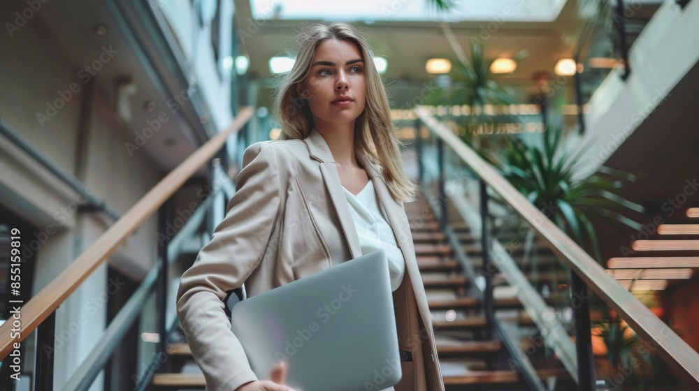 A Young Businesswoman Walking Down The Stairs, Holding A Laptop, Focused On Her Tasks A Young Businesswoman Walking Down The Stairs, Holding A Laptop, Focused On Her Tasks