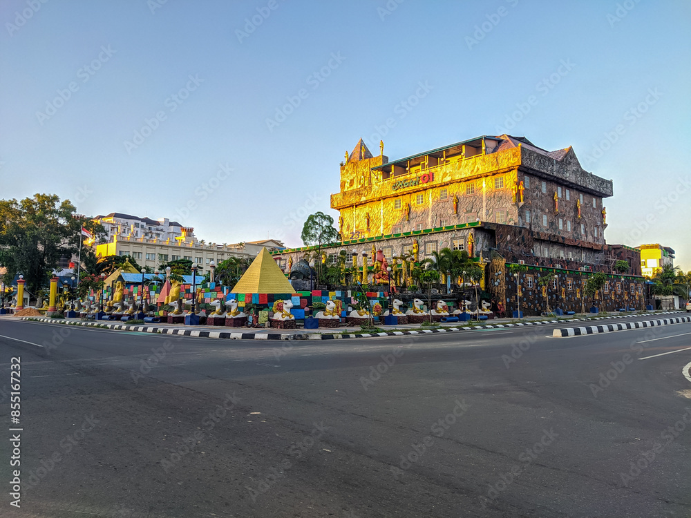 Unique castle-like hotel in Batam city, adorned with colorful decorations and a small pyramid at its base, standing prominently on a street corner under a clear blue sky