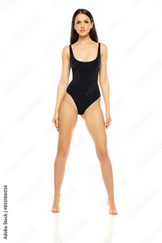 Young brunette woman in one piece bikini swimsuit posing on a whitestudio background. Front view. Young brunette woman in one piece bikini swimsuit posing on a whitestudio background. Front view.