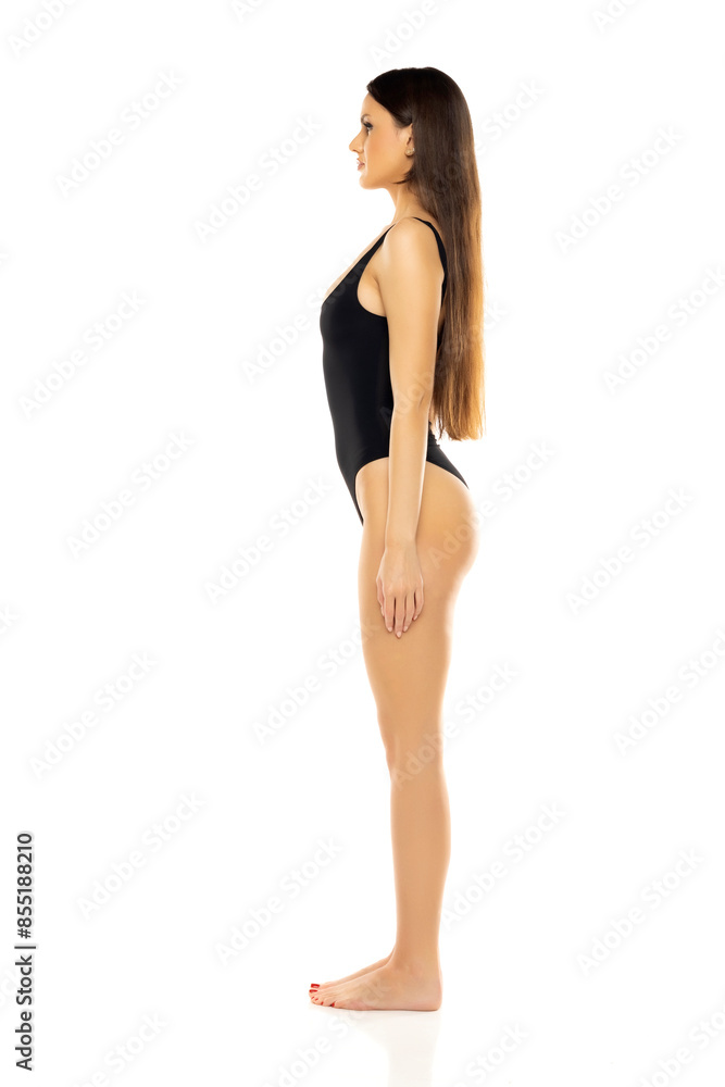 Young brunette woman in one piece bikini swimsuit posing on a white studio background. Side view Young brunette woman in one piece bikini swimsuit posing on a white studio background. Side view