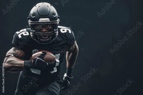 American football player in black uniform running with the ball, captured in an action shot against a dark background