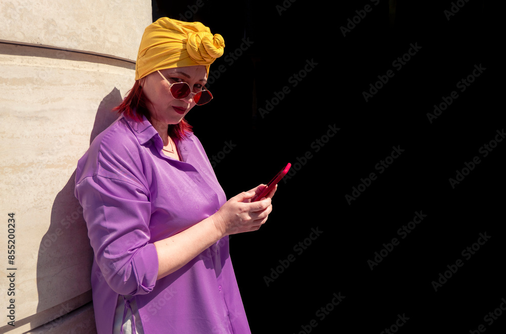 Happy and funny cool lady with fashionable clothes on dark background look to the phone seriously and thoughtfully - adult asian with extravagant style isolated on black background