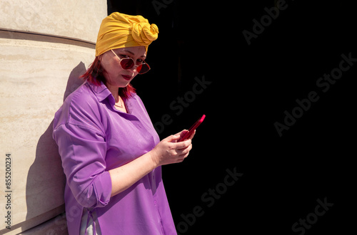Obraz na płótnie Happy and funny cool lady with fashionable clothes on dark background look to the phone seriously and thoughtfully - adult asian with extravagant style isolated on black background w salonie