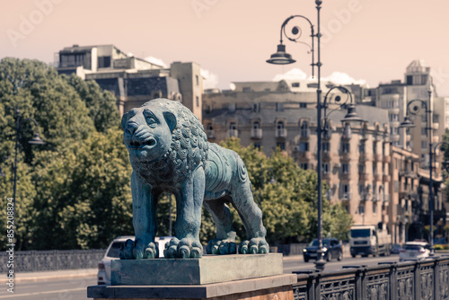 Day cityscape with lion sculpture on bridge fence and view to modern city buildings, Tbilisi, Georgia photo