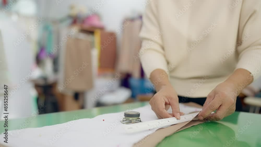 A woman is cutting fabric with a pair of scissors. She is wearing a white shirt and black pants A woman is cutting fabric with a pair of scissors. She is wearing a white shirt and black pants