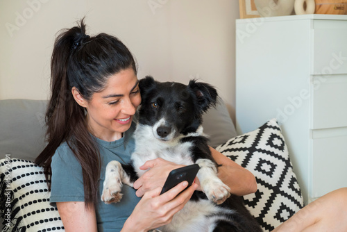 Beautiful  young woman sitting at home ,hugging her adopted dog and  using mobile phone