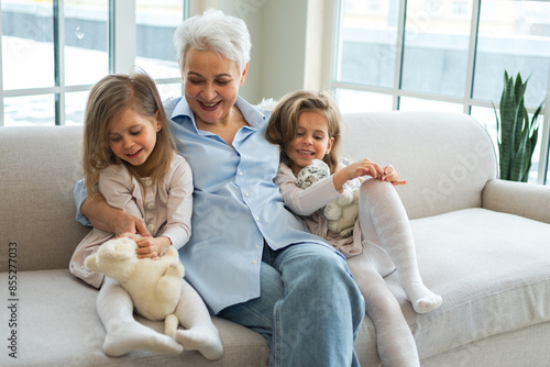 Happy family at home. Two little girls sisters twins grandmother enjoying time together. Good time at home. Grandma granddaughters child kids emotional bonding hugging together. Family generations