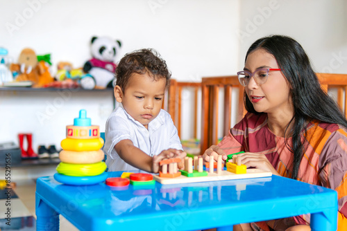 Son focused while playing at home with his young mother, both are Latino, and many toys are seen in the background
