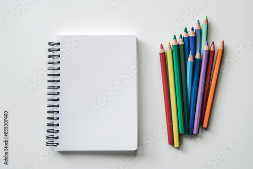 Top view of colorful pencils and blank spiral workbook on white background, perfect for creative projects photo