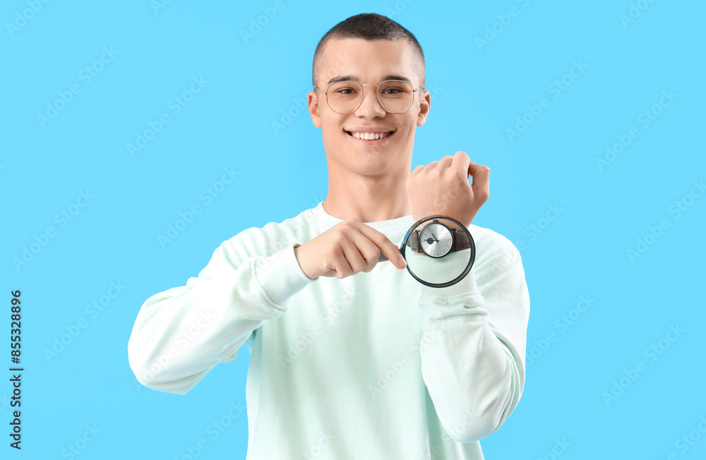 Young man with watch and magnifier on blue background