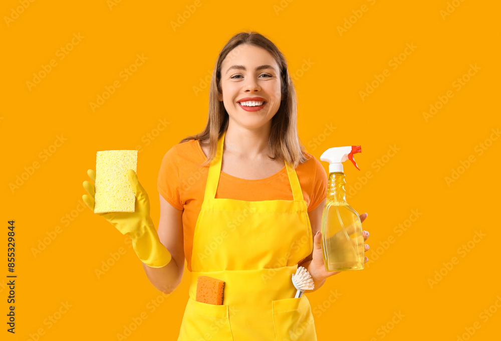 Young woman with bottle of detergent and cleaning sponge on orange background Young woman with bottle of detergent and cleaning sponge on orange background