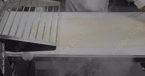 Fresh dough coming out of a dough sheeter rolling machine in a bakery kitchen. Croissant pasta phyllo dough photo
