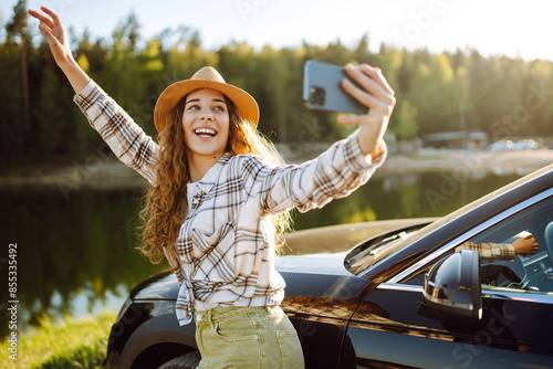 Young female tourist traveling by car taking selfie. Rest stop in car trip to take photos. Active lifestyle, blogging, nature, weekend.