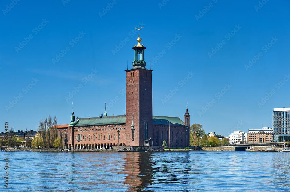 Stockholm City Hall with its red brick facade and tower on Kungsholmen Island, and Lake Malar with Riddarfjärden Bay or Gulf of Knights in the foreground Stockholm City Hall with its red brick facade and tower on Kungsholmen Island, and Lake Malar with Riddarfjärden Bay or Gulf of Knights in the foreground
