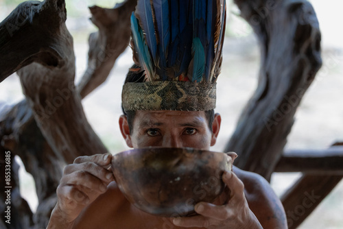 Indigenous Wayuri Man Drinking Chicha from Bowl Wearing Feather Crown in Puyo, Ecuador photo
