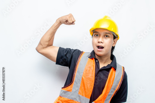 ecstatic asian male construction worker in yellow hardhat and orange vest raising his fist showing his success and celebrating his achievments. photo