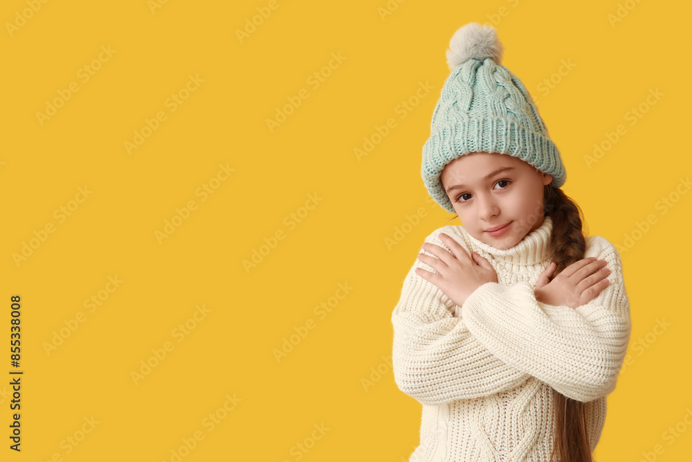 Cute little girl in warm hat hugging herself on yellow background Cute little girl in warm hat hugging herself on yellow background